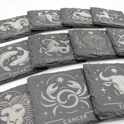 Set of slate coasters with zodiac designs on a white surface