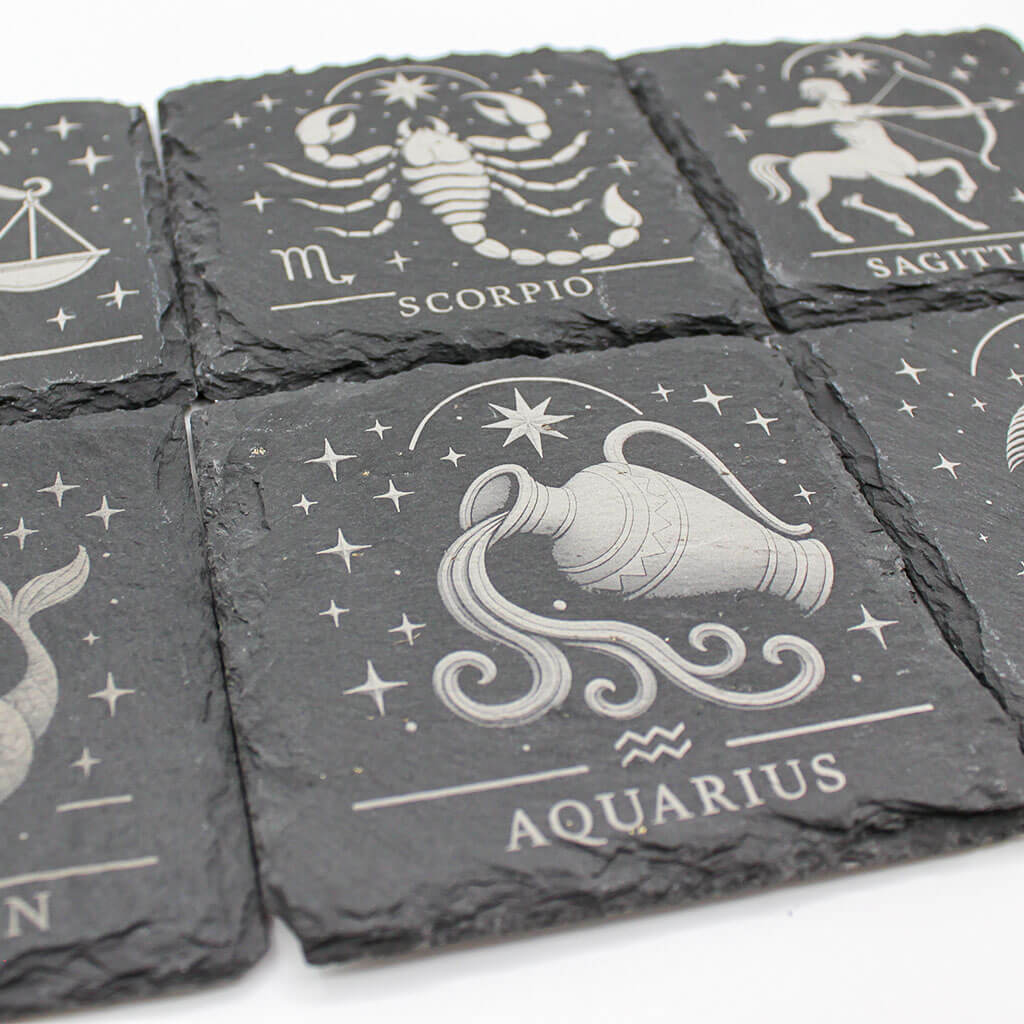 Set of six slate coasters with zodiac designs on a white background