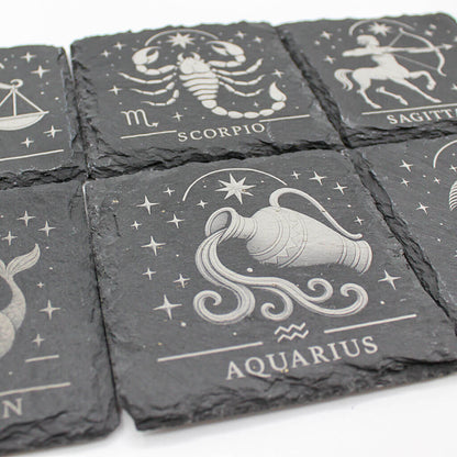 Set of six slate coasters with zodiac designs on a white background